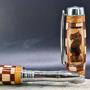May include: A wooden pen with a chess knight design. The pen features a checkered pattern in light and dark wood, with a silver metal tip and clip. The pen's cap showcases a detailed knight silhouette.