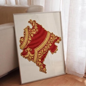 Könnte beinhalten: Gerahmtes Kunstwerk mit einer rot-goldenen, gestickten Karte eines Landes. Die Karte ist mit aufwendigen Goldmustern versehen und in einem silbernen Metallrahmen gerahmt. Das Kunstwerk wird vor einem weißen Hintergrund präsentiert.