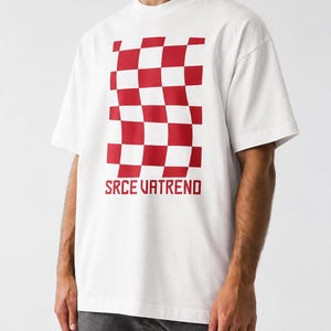 May include: A white short-sleeve t-shirt featuring a red and white checkered pattern that appears distorted or wavy in the center. Below the graphic, the text SRCE VATREND is printed in a bold, red, sans-serif font on the chest area.