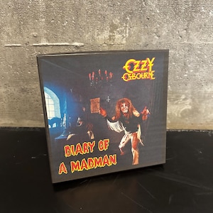 May include: A square box featuring the album cover for Ozzy Osbourne's "Diary of a Madman." The artwork depicts a horror scene with a figure holding a scroll. The Ozzy Osbourne logo is at the top right.