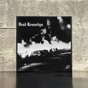 May include: Black and white album cover featuring the band name "Dead Kennedys" in a gothic font. The image depicts a burning vehicle with figures in the foreground, creating a dramatic and punk rock aesthetic.