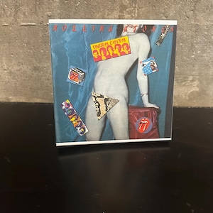 May include: Album cover for The Rolling Stones' "Undercover" album. The cover features a nude figure with various patches and the band's name at the top. The album cover is on a black surface.