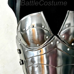 May include: A shiny, silver-coloured breastplate with riveted detailing. The armour has a curved design and is displayed on a black mannequin. The text "BattleCostume" is visible on the upper left.