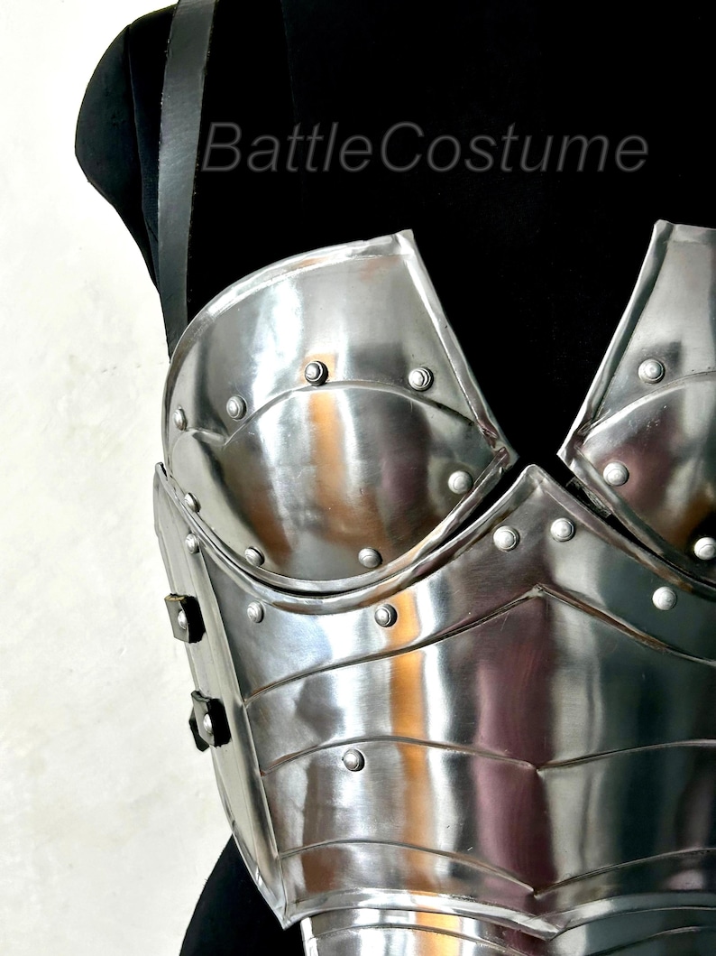 May include: A shiny, silver-coloured breastplate with riveted detailing. The armour has a curved design and is displayed on a black mannequin. The text "BattleCostume" is visible on the upper left.