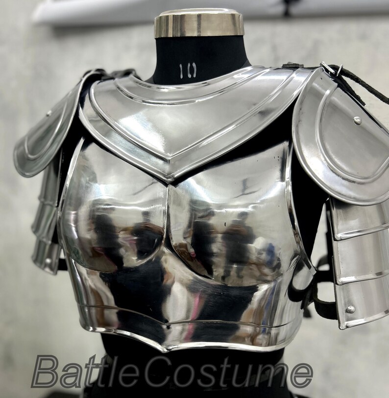 May include: A polished, silver-colored breastplate and shoulder armor set. The armor is displayed on a black mannequin and features articulated shoulder guards and a chest plate with a reflective surface. The text "BattleCostume" is visible at the bottom.