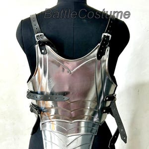 May include: A polished silver breastplate with black leather straps and buckles. The armour is displayed on a black mannequin. The text "Battle Costume" is visible on the mannequin.