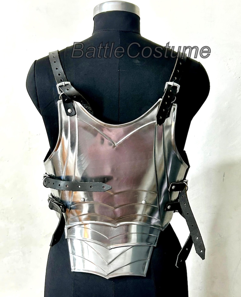 May include: A polished silver breastplate with black leather straps and buckles. The armour is displayed on a black mannequin. The text "Battle Costume" is visible on the mannequin.
