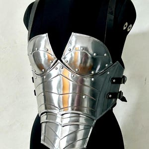 May include: A silver breastplate with riveted detailing and black leather straps, displayed on a black mannequin. The text "Battle Costume" is visible at the bottom of the image.