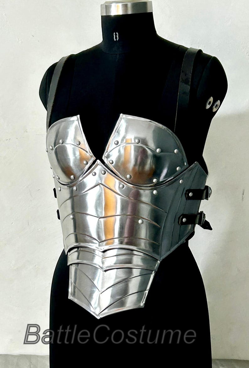 May include: A silver breastplate with riveted detailing and black leather straps, displayed on a black mannequin. The text "Battle Costume" is visible at the bottom of the image.