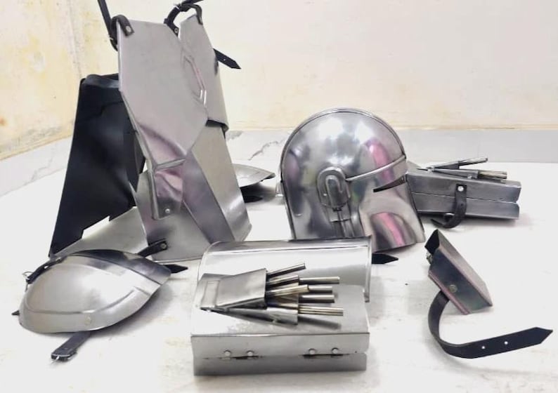 May include: A collection of silver-colored metal armor pieces, including a helmet, chest plates, and arm guards. The armor appears to be new and unused, with straps and hinges visible for assembly. The pieces are arranged on a light-colored surface.