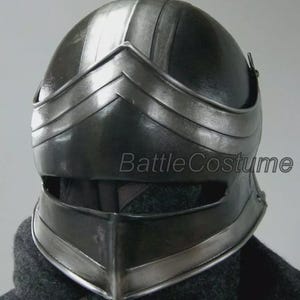 K&ouml;nnte beinhalten: Ein schwarzer mittelalterlicher Helm mit Visier und abgerundeter Oberseite. Der Helm hat silberfarbene Verzierungen und der Text "BattleCostume" ist auf der Seite sichtbar. Der Helm ist f&uuml;r Kost&uuml;me oder Cosplay konzipiert.