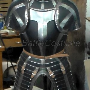 May include: A full suit of medieval armour, with a black and silver design. The armour includes a chest plate, shoulder guards, and leg protection, all connected with leather straps. The text "BattleCostume" is visible on the chest.