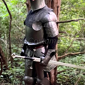 May include: A full suit of medieval armor, including a helmet, chainmail, and plate armor, is displayed. The armor is a dark metallic color and includes a sword. The image is set in a natural outdoor environment.