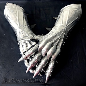 May include: Silver metal gauntlets with detailed engraved patterns and sharp, pointed claws. The gauntlets have articulated sections and protective plates, suitable for cosplay or costume use. The text "Battlecostume" is visible at the bottom.