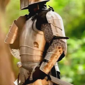 K&ouml;nnte beinhalten: Eine mittelalterliche Ritterr&uuml;stung mit Helm, Brustpanzer und Armsch&uuml;tzern. Die R&uuml;stung ist silberfarben mit Kettengeflecht-Akzenten. Ein Schwert wird an der Seite des Ritters gehalten. Der Hintergrund ist verschwommen gr&uuml;n und braun.