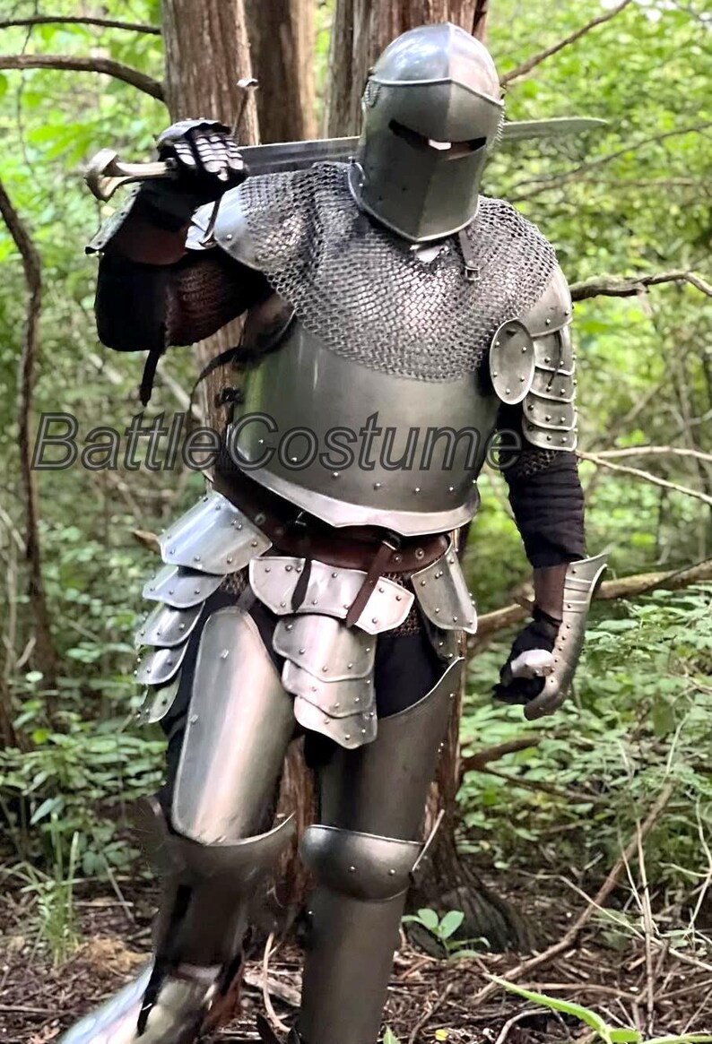 May include: A full suit of medieval armor, including a helmet, chainmail, and plate armor, with a sword resting on the shoulder. The armor is silver-colored and worn in a forest setting. The text "Battle Costume" is visible.