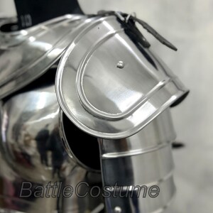 May include: Polished silver shoulder armor with layered plates and a curved design. The armor is displayed on a black mannequin and features a leather strap. The text "BattleCostume" is visible on the armor.
