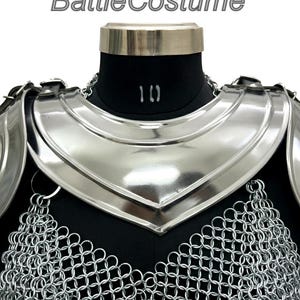 Puede incluir: Peto de armadura medieval plateado con acabado pulido. La armadura incluye una secci&oacute;n de cota de malla y un protector de cuello. El texto "BattleCostume" es visible en la parte superior.