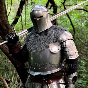 May include: A full suit of medieval armor, including a helmet, chainmail, and plate armor, with a long sword resting on the shoulder. The armor is silver-colored and appears to be made of metal. The text "BattleCostume" is visible on the armor.