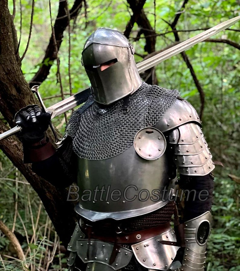 May include: A full suit of medieval armor, including a helmet, chainmail, and plate armor, with a long sword resting on the shoulder. The armor is silver-colored and appears to be made of metal. The text "BattleCostume" is visible on the armor.