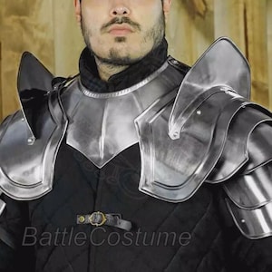 Könnte beinhalten: Silberfarbene Schulterpanzer aus Stahl mit geschichteten Platten und hohem Kragen. Die Rüstung wird über einem schwarzen, gesteppten Kleidungsstück getragen. Der Text "BattleCostume" ist sichtbar.