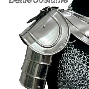 Puede incluir: Primer plano de una armadura de hombro medieval plateada con cota de malla. La armadura tiene un acabado pulido y est&aacute; hecha de metal. El texto "BattleCostume" es visible en la esquina superior izquierda.