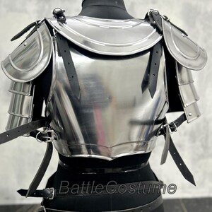 May include: A polished steel breastplate and shoulder armor set, featuring articulated shoulder plates and leather straps for attachment. The armor is displayed on a black mannequin, showcasing its reflective surface and intricate design.