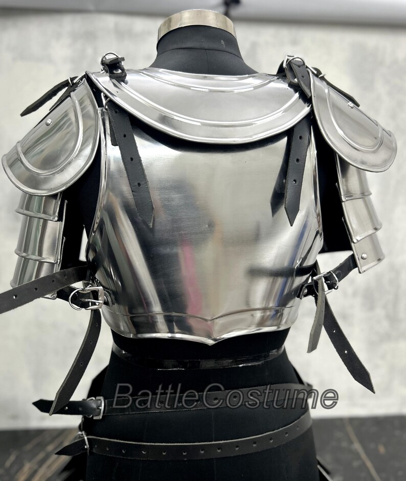 May include: A polished steel breastplate and shoulder armor set, featuring articulated shoulder plates and leather straps for attachment. The armor is displayed on a black mannequin, showcasing its reflective surface and intricate design.