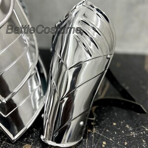 May include: Highly polished silver metal arm armor with riveted accents. The armor has a reflective surface and is designed with a series of angled plates. The text "BattleCostume" is visible on the armor.