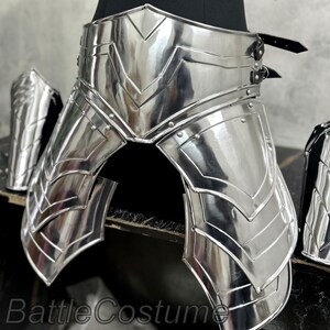 May include: Shiny silver metal armor set, including a waist belt, leg guards, and arm guards. The armor has a detailed, layered design with riveted accents. The text "BattleCostume" is visible at the bottom.