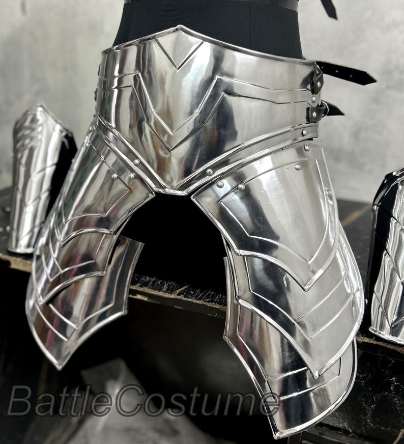 May include: Shiny silver metal armor set, including a waist belt, leg guards, and arm guards. The armor has a detailed, layered design with riveted accents. The text "BattleCostume" is visible at the bottom.