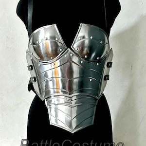 May include: A silver metal breastplate, displayed on a black mannequin. The armour features a detailed design with rivets and layered plates. The text "Battle Costume" is visible at the bottom of the image.