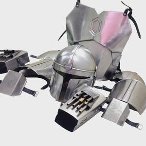 May include: A silver-colored Mandalorian armor set, including a helmet, chest plate, shoulder pads, and gauntlets. The armor has a metallic finish and is designed with detailed panels and straps. The helmet features a T-shaped visor.