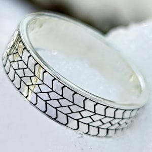 May include: A silver ring with a geometric tire tread pattern. The ring is set against a snowy background, with the words "JEWELRY ETERNITY" in a circular design.