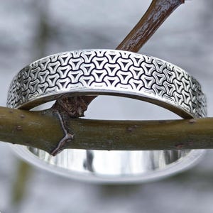 May include: Two silver rings, one with a geometric pattern, rest on a tree branch. The rings are displayed against a blurred, snowy background. The rings are part of the "Jewelry Eternity" collection.