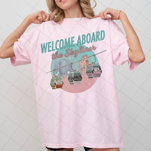 Peut inclure: T-shirt rose clair avec l'inscription "WELCOME ABOARD the Skyliner" en turquoise. Le motif représente trois télécabines, un globe et un bâtiment. Le t-shirt est à col rond et à manches courtes.