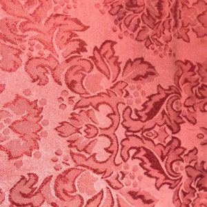 May include: Close-up of a red fabric with a damask pattern. The pattern is in a darker red color and features intricate floral designs.