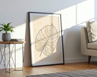 Könnte beinhalten: Ein gerahmter Kunstdruck mit einer großen Blattillustration mit schwarzen Umrissen auf beigem Hintergrund. Das Kunstwerk lehnt an einer weißen Wand, neben einem kleinen Beistelltisch aus Holz mit einer Topfpflanze und Büchern. Der Raum hat Holzböden.