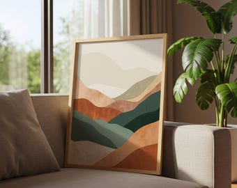 May include: A framed art print featuring an abstract landscape with layered hills in shades of beige, rust, and green. The artwork is displayed on a beige sofa, with a large houseplant in the background. The frame is made of light-colored wood.