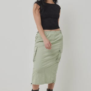May include: A woman in a black textured cap-sleeve top and a light green cargo midi skirt, paired with black combat boots. The outfit is set against a plain white background. The skirt is approximately 76 cm in length.