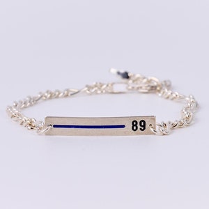 May include: Silver chain bracelet with a thin silver bar charm. The bar has a blue stripe and the number 89 engraved on it.