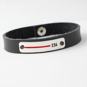 May include: Black leather bracelet with a silver rectangular tag that has a red line and the number 234.