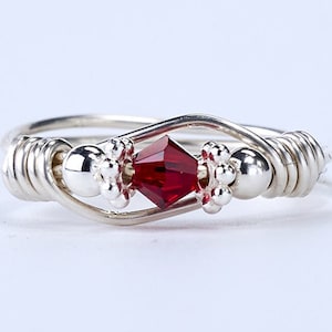 May include: A silver ring with a red crystal and silver beads. The ring is made of wire that is wrapped around itself.