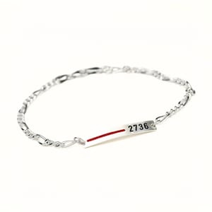 May include: A silver chain bracelet with a silver tag that has a red stripe and the number "2736" printed on it.
