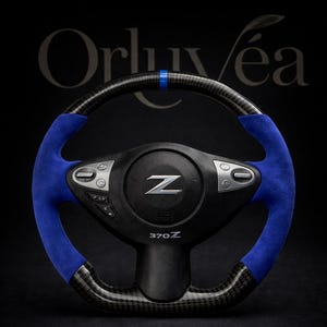May include: A custom steering wheel with a carbon fiber and blue suede design. The wheel features a black center with the letter "Z" and the text "370Z". The top of the wheel has a blue stripe.