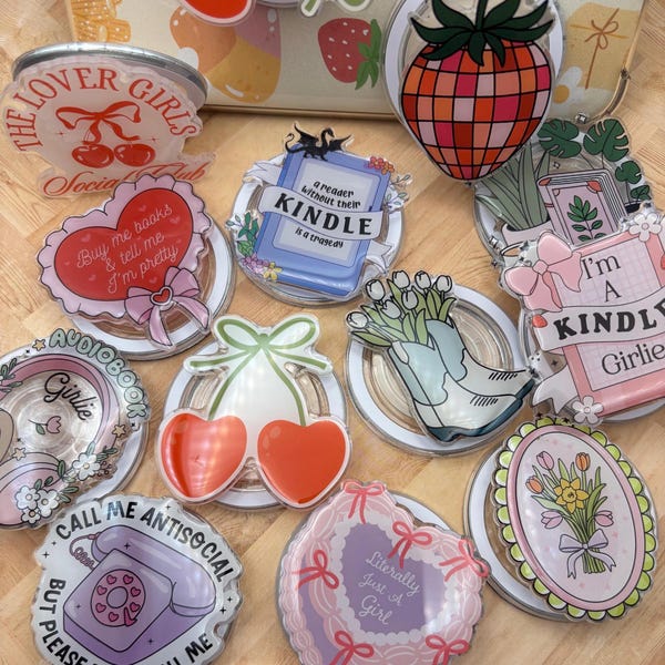 May include: A collection of clear acrylic coasters with various designs and text. Designs include cherries, strawberries, a book, a telephone, and floral arrangements. Text includes "The Lover Girls", "Buy me books & tell me I'm pretty", and "Call me antisocial".