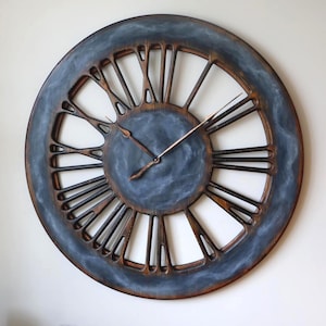 May include: Large, round wall clock with a distressed, industrial design. The clock features a dark blue face with Roman numerals and a weathered, brown wooden frame. The clock hands are a copper color.