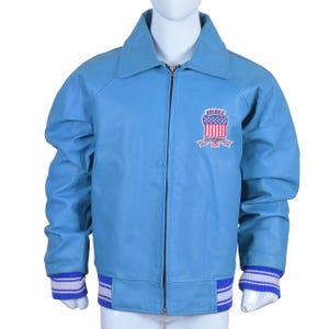 May include: Light blue leather jacket with a zip-up front, a collar, and ribbed cuffs and hem. The jacket features a patch on the chest with the text "AVIREX" and a design of red and white stripes. The cuffs and hem have white and blue stripes.