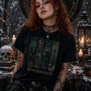 May include: A black t-shirt featuring a graphic print divided into four vertical panels depicting dark, winter-themed scenes with a crescent moon and the text Krampusnacht printed in a gothic font at the bottom of the graphic design.