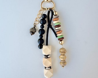May include: A decorative keychain with a gold-colored clasp and various charms. The charms include black beads, wooden geometric shapes, and a small acorn pendant. Additional charms feature a mix of colorful beads and gold accents.